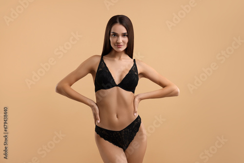 Young woman in elegant black underwear on beige background