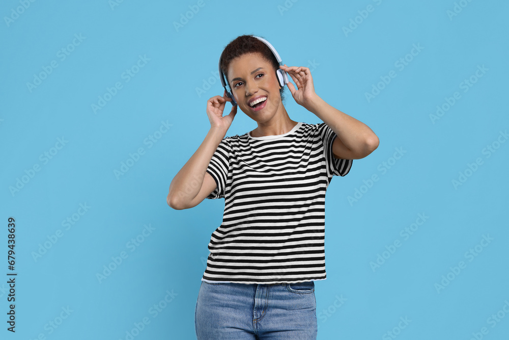 Happy young woman in headphones dancing on light blue background Happy young woman in headphones dancing on light blue background