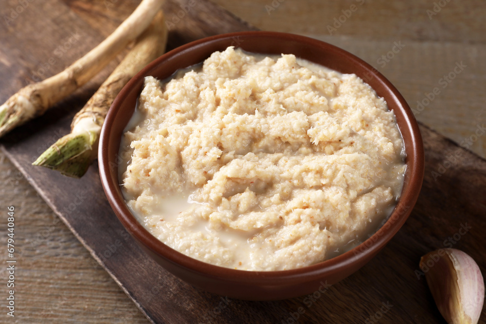 Spicy horseradish sauce in bowl, roots and garlic on wooden table, closeup Spicy horseradish sauce in bowl, roots and garlic on wooden table, closeup