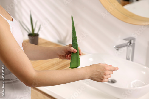 Fototapeta Naklejka Na Ścianę i Meble -  Young woman applying aloe gel from leaf onto her arm in bathroom, closeup