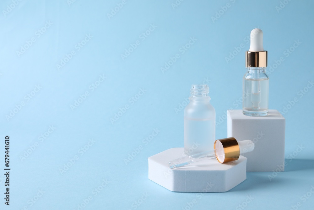 Presentation of bottles with cosmetic serums on light blue background, space for text Presentation of bottles with cosmetic serums on light blue background, space for text