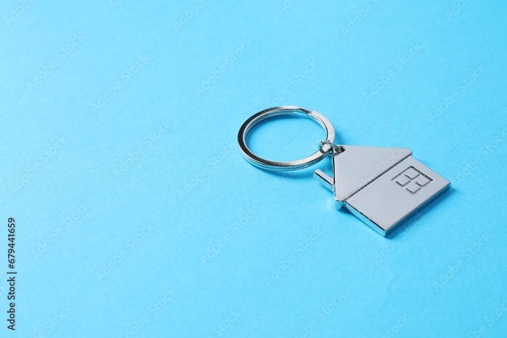 Metallic keychain in shape of house on light blue background. Space for text Metallic keychain in shape of house on light blue background. Space for text