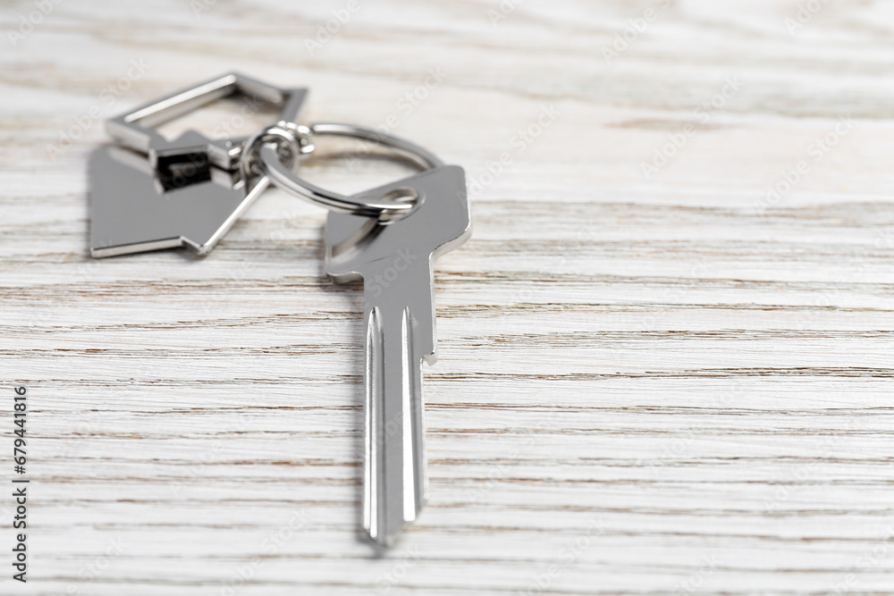 Key with keychain in shape of house on light wooden table, closeup. Space for text Key with keychain in shape of house on light wooden table, closeup. Space for text