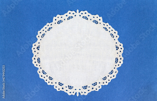Round white table napkin with cutwork embroidered lace edge on a blue background. Blank space for text. Close-up, top view, copy space, flat lay, mock up photo