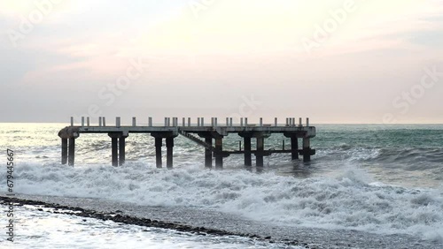 Waves crash against an old, destroyed pier. There is no connection with the shore. A storm warning. Bad weather and old architecture