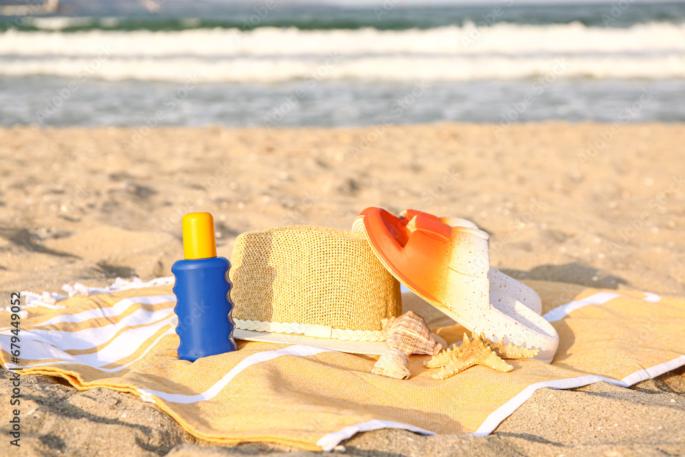 Towel with stylish hat, flip-flops and bottle of sunscreen cream on sand Towel with stylish hat, flip-flops and bottle of sunscreen cream on sand