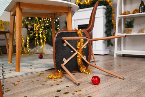 Fallen chair with tinsel in messy living room after New Year party