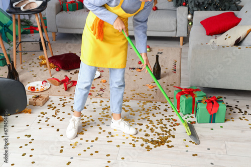 Female janitor sweeping floor in messy living room after New Year party photo
