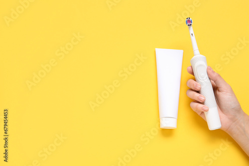 Female hand with toothbrush and toothpaste on turquoise background.