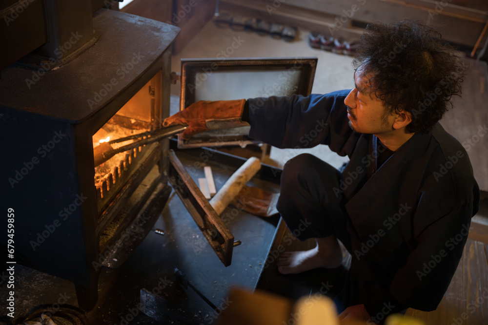 A man putting firewood into a wood stove Image of winter preparation in the countryside in a Japanese winter A bird's eye view of real, careful living A man putting firewood into a wood stove Image of winter preparation in the countryside in a Japanese winter A bird's eye view of real, careful living