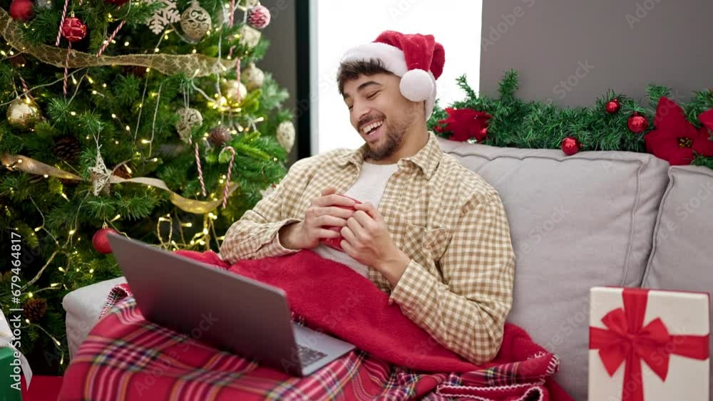 Young arab man watching movie drinking coffee sitting by christmas tree at home Young arab man watching movie drinking coffee sitting by christmas tree at home