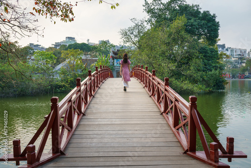 Red bridge The Huc in Hoan Kiem lake, Hanoi, with a girl in long dress walking on the bridge photo