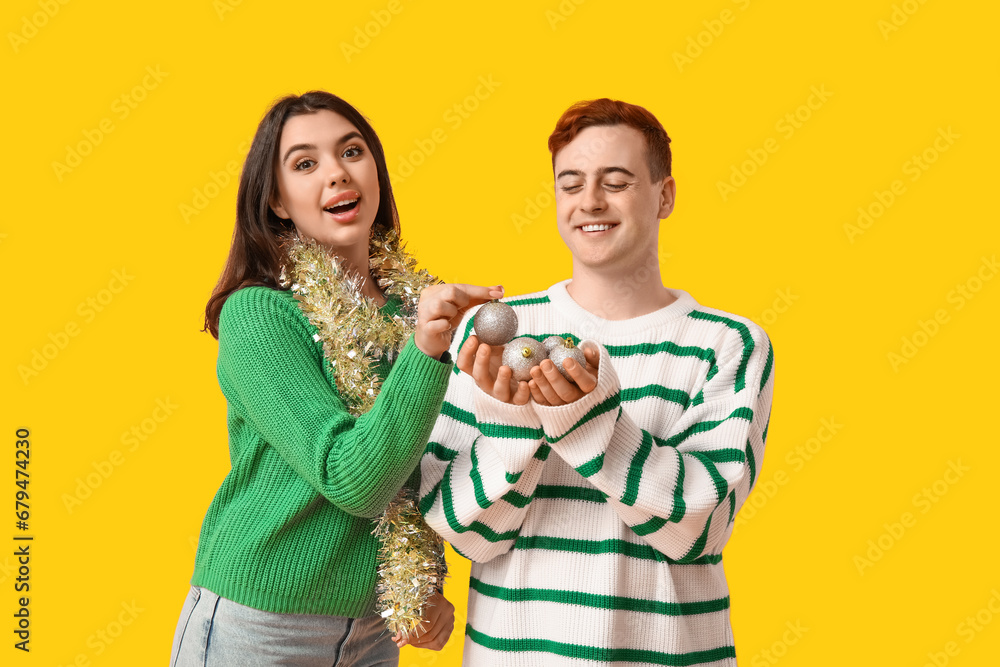 Young couple with Christmas tinsel and balls on yellow background Young couple with Christmas tinsel and balls on yellow background