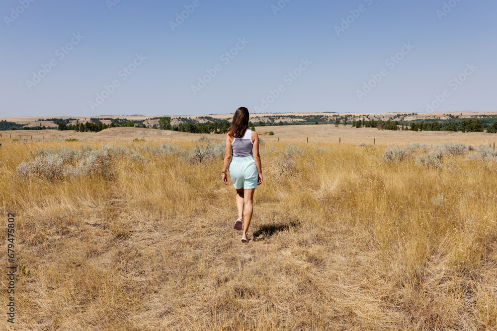 A young girl with brown hair in green shorts walks through a meadow with dry grass on a sunny autumn day