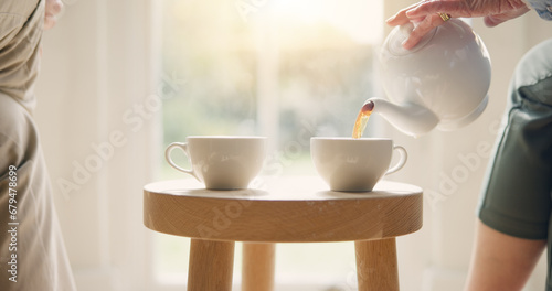 Pot, pour and hands with tea cup in morning, home and closeup on drink, steam and table. Hot, beverage and person with hospitality, service and drinking in the afternoon with friends in living room photo
