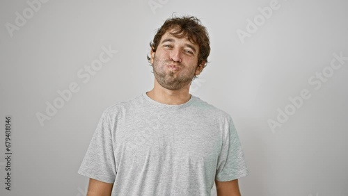 Cheeky young guy in a t-shirt making a hilarious grimace, puffing cheeks full of air for a crazy fun face. standing isolated, he breathes life into the white background. photo