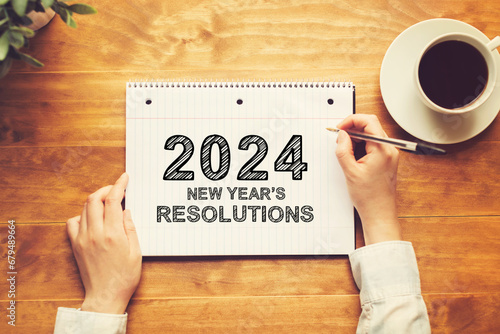 2024 New Years Resolutions with a person holding a pen on a wooden desk