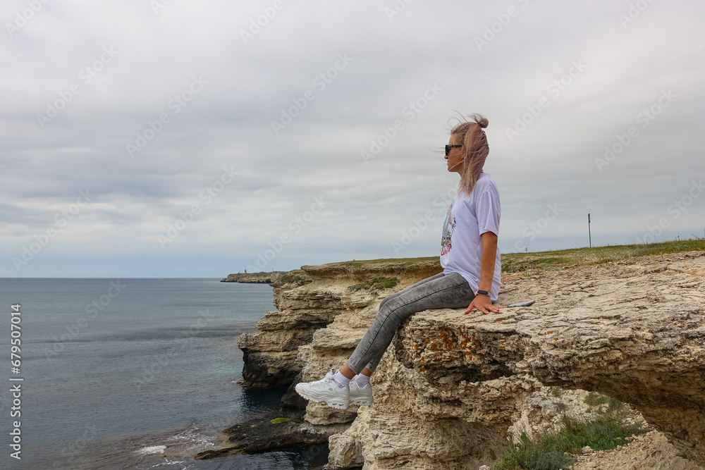The girl at Cape Tarkhankut. The rocky coast of the Dzhangul Reserve in the Crimea. Turquoise sea water. Rocks and grottoes of Cape Tarkhankut on the Crimean peninsula.
