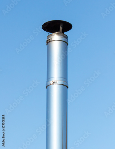 Metal exhaust pipe on the wall of a building. Against a background of blue sky