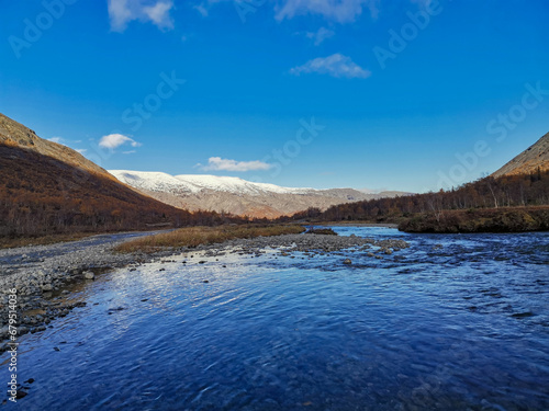 Golden autumn in the Arctic mountains beyond the Arctic Circle. View of a beautiful lake and yellow birches. Mountain peaks in the background. Autumn in the mountains of Khibiny.