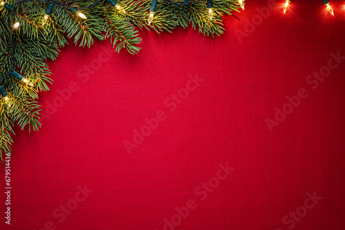 Red fabric texture framed by Christmas tree twig with lights. Christmas texture background
