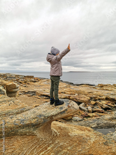 A boy on the shore of red stones next to the rocks of Two brothers on the Fishing Peninsula. The picturesque shore of the harsh Barents Sea. The North of Russia. The Kola Peninsula. The Arctic