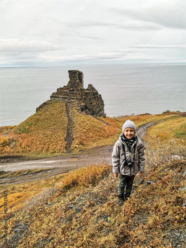 A boy against the background of Two brothers rocks near Cape Zemlyanoi on the Kola Peninsula. Natural weathering pillars. The rocky coast of the Barents Sea. The ancient sanctuary of the Sami.
