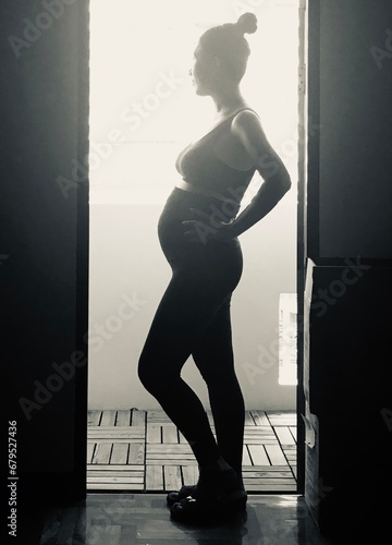 silhouette of a pregnant woman standing at opening door