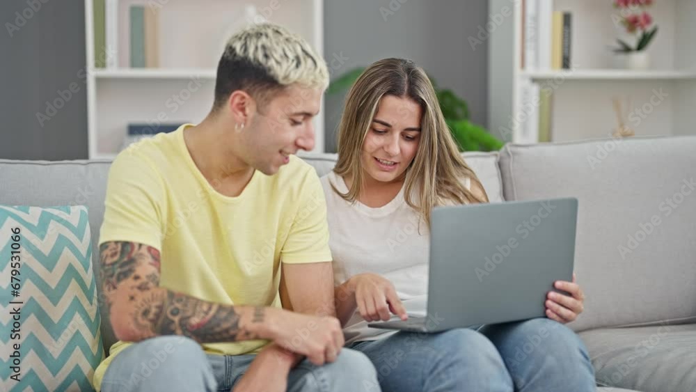 Beautiful couple using laptop sitting on sofa celebrating at home Beautiful couple using laptop sitting on sofa celebrating at home