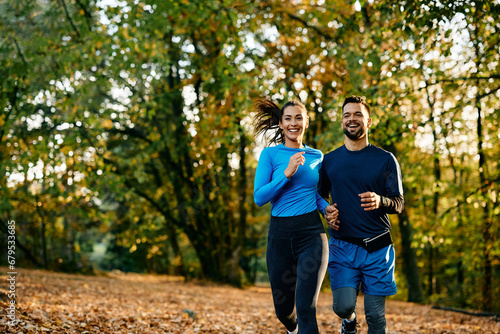 Happy couple of athletes running in autumn day in nature.
