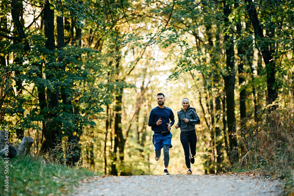 Happy couple of athletes jogging while working out in park.