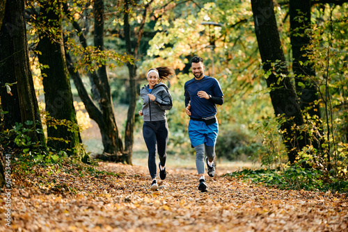 Young athletic couple jogging during autumn day in park.