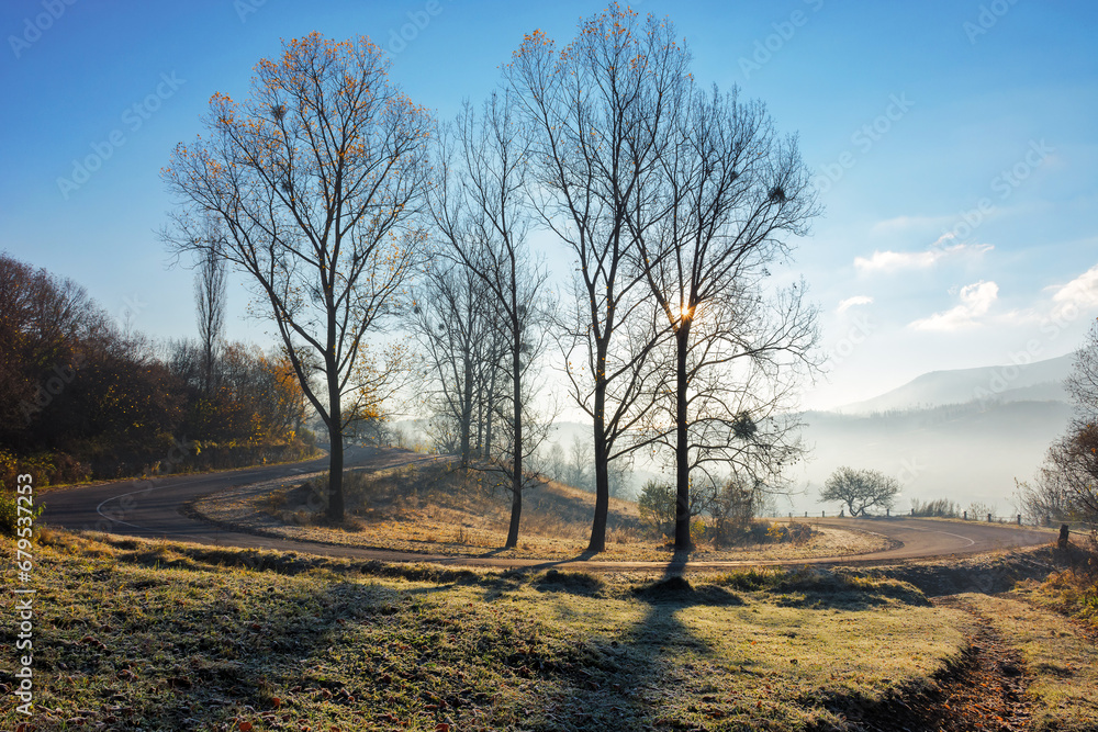 mountain pass in autumn. sun behind the leafless trees on the grassy hills in frost. mist in the valley. blue sky above the distant ridge mountain pass in autumn. sun behind the leafless trees on the grassy hills in frost. mist in the valley. blue sky above the distant ridge