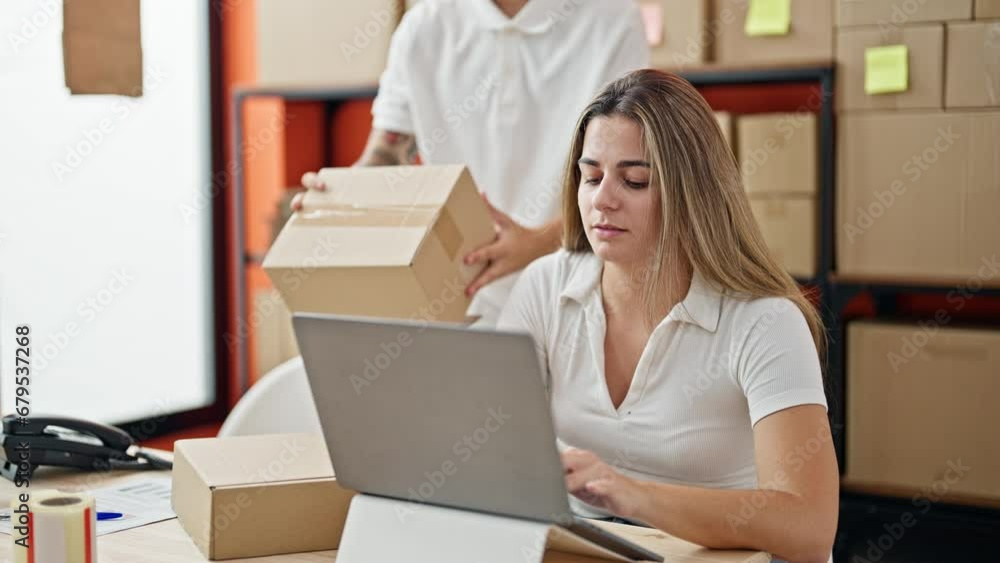 Two workers man and woman using laptop checking package at office Two workers man and woman using laptop checking package at office