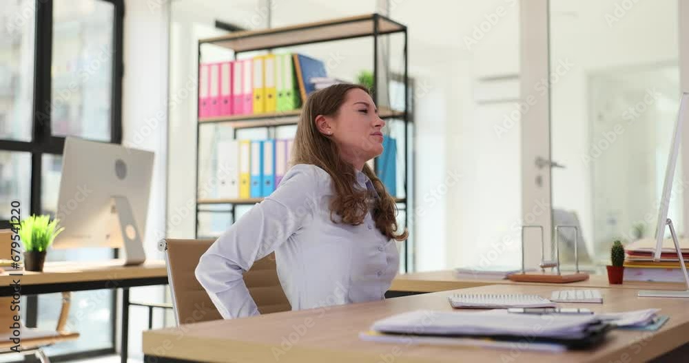 Woman sitting in office and having problems with posture and back working at computer Woman sitting in office and having problems with posture and back working at computer
