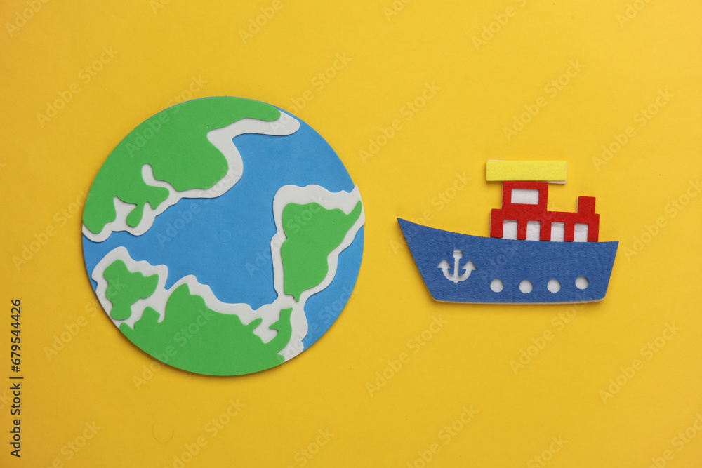Toy ship made of felt and globe on a yellow background. Travel concept