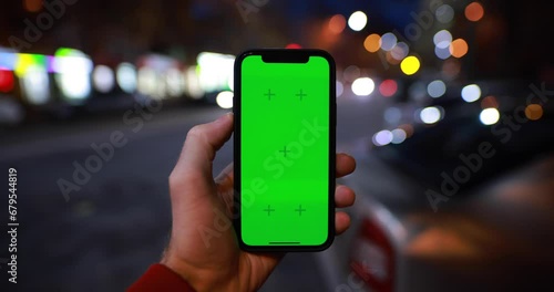 POV male hand holding smartphone with green screen chroma key near night road