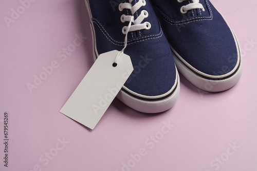 Old school sneakers with a white blank tag on a string, purple background. Template for design, sale, shopping concept
