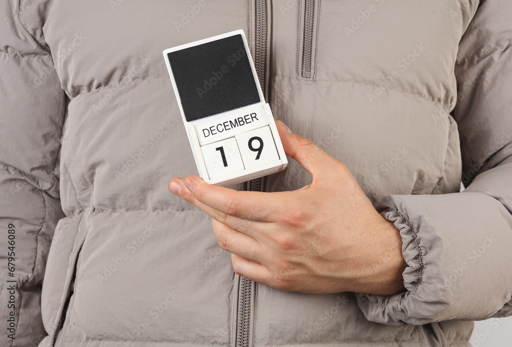 Man in down jacket holds wooden block calendar with date December 19 Man in down jacket holds wooden block calendar with date December 19