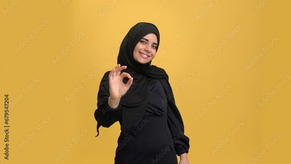 Beautiful Arabic young woman black hijab showing ok okay good gesture posing isolated orange studio Beautiful Arabic young woman black hijab showing ok okay good gesture posing isolated orange studio