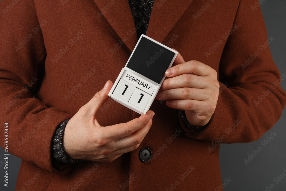 Man in woolen coat holds calendar with the date february 11 Man in woolen coat holds calendar with the date february 11