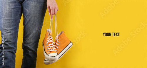 Woman holds yellow retro 80s rubber sneakers by the laces on a yellow background. Fashion concept. Copy space photo