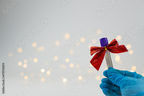 Christmas in laboratory. Hand in blue glow show medical test tubes with christmas bows and christmas lights on background photo