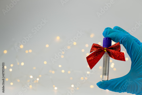 Christmas in laboratory. Hand in blue glow show medical test tubes with christmas bows and christmas lights on background