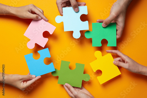 Сolored puzzles in hands on orange background, top view