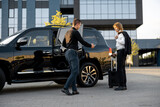 Chauffeur helps businessman with a suitcase to get in the car, opening a door of a luxury black taxi. Man having a business trip