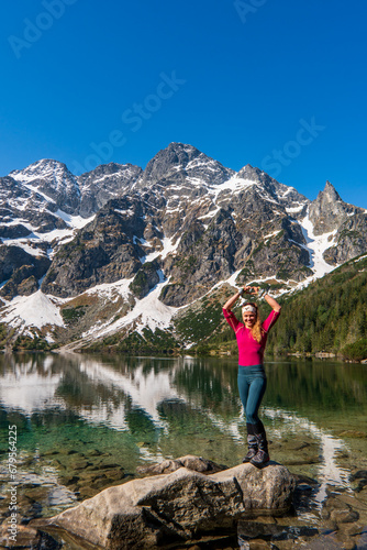 a woman stands and shows a heart by a beautiful lake in the mountains. Famous mountains lake Morskie oko or sea eye lake In High Tatras. Five lakes valley