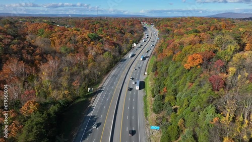 Interstate highway in America during autumn. Aerial shot above traffic traveling on freeway cutting between colorful forest foliage.