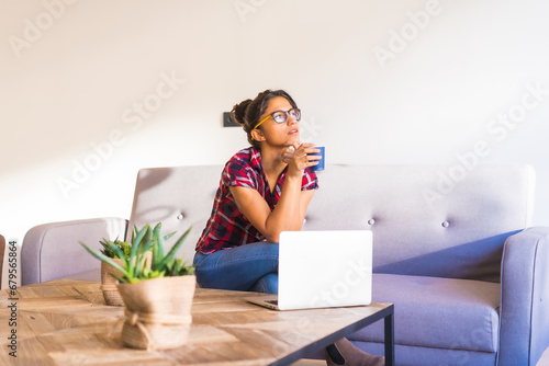 Pensive woman drinking coffee and using laptop at home