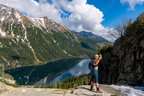 woman standing over the lake and taking a selfie in the mountains, Beautiful Eye of the Sea lake in Tatra mountains, Poland